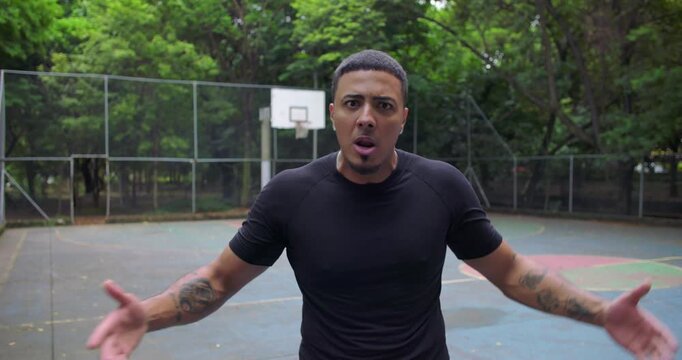 Frustrated African American man arguing and raising hand toward camera during heated dispute on outdoor basketball court, intense expression and emotional tension