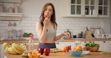 Young woman in activewear making organic fruit smoothies drink in a bright modern kitchen at home. Asian girl preparing healthy food. Natural clean diet and wellness lifestyle.