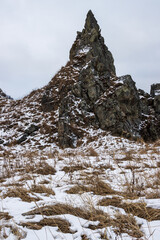 View of a high rock with a sharp peak. Majestic mountain landscape. Cold winter weather. Snow-covered ground and rocks. Beautiful nature of Siberia and the Russian Far East. Magadan region. Russia.