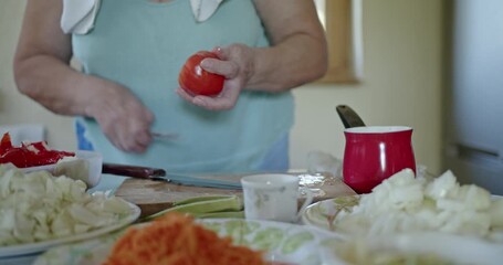 A close-up shot captures the meticulous process of a senior woman peeling a fresh red tomato in her kitchen. - Powered by Adobe
