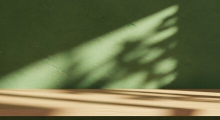 Empty wooden surface with dappled natural sunlight and plant shadows on a textured green wall, creating a peaceful and versatile backdrop for product presentations