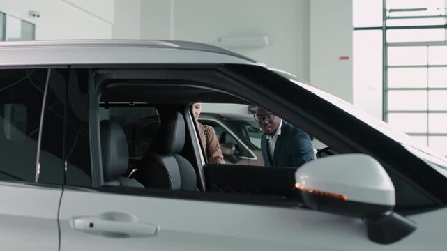 A female buyer and male salesperson discuss vehicle specifications in a dealership showroom, demonstrating customer interaction and the buying experience in the modern automotive environment.