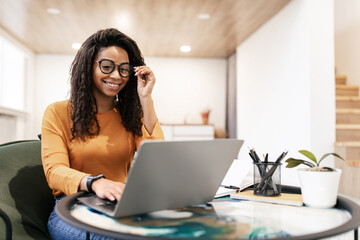 A woman with curly hair is seated at a table, engaged in her work on a laptop while wearing...