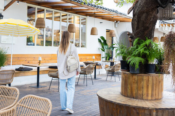 Young woman with backpack walking through outdoor cafe seating area