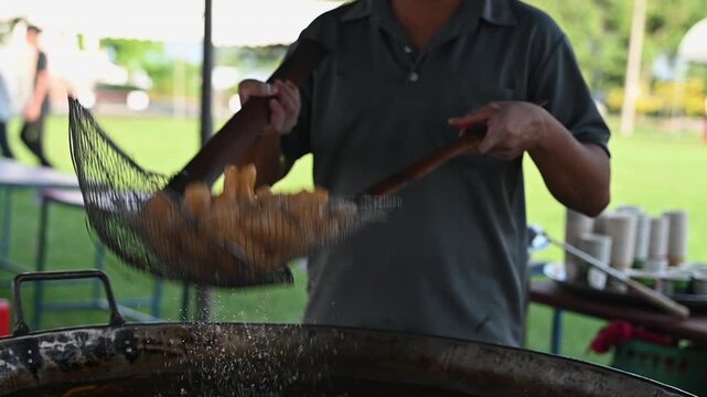 Golden fried dough stick pastry snack slow motion over hot oil, street food vendor outdoor market morning scene, crispy texture and oil droplets sparkle, handheld daylight shot with bamboo strainers