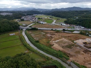 A rural area with a river running through it. The river is surrounded by fields and trees. The sky is cloudy and the overall mood of the image is peaceful and serene