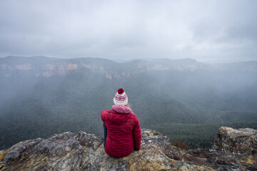 Woman sitting on cliff in Blue Mountains, with mist and fog