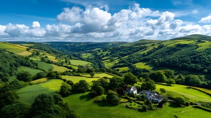 Rolling green hillsides with scattered trees and a cluster of white buildings stretch beneath a bright blue sky dotted with clouds.