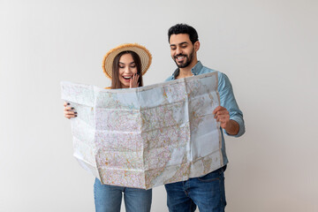 A young couple looks at a detailed map, excited about their travel plans. They share a joyful...