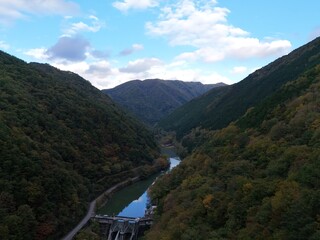 A river runs through a lush green valley with a mountain range in the background. The sky is clear...