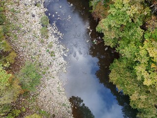 A river with a rocky bank and a clear blue sky. The water is calm and peaceful. The trees on the...
