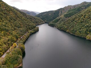 A beautiful lake surrounded by trees and mountains. The water is calm and clear. The sky is cloudy, but the sun is still shining through the clouds. The scene is peaceful and serene