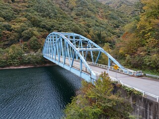 A bridge spans a river with a blue color. The bridge is surrounded by trees and the water is calm