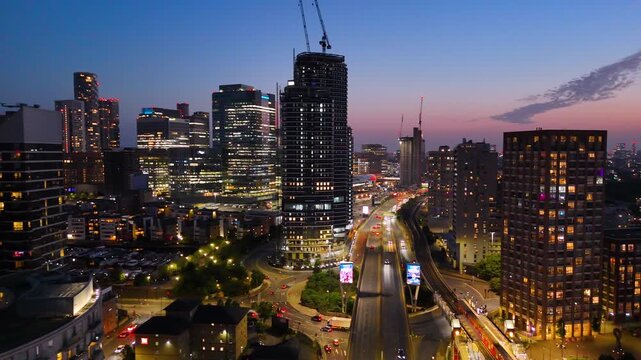 Night aerial views of London&rsquo;s skyline, showcasing illuminated towers, highways, trains, and vibrant urban lights during twilight. Cinematic city atmosphere.