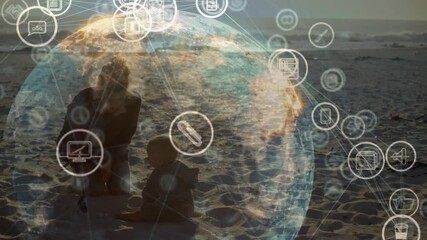 Woman guiding toddler scooping sand and causing technology icons forming data globe at sunset - Powered by Adobe