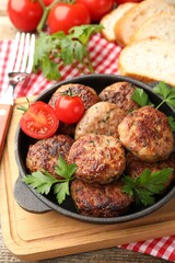 Delicious patties with parsley and tomatoes in pan on wooden table
