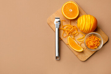 Orange zest, fresh fruits and zester tool on beige background, top view. Space for text