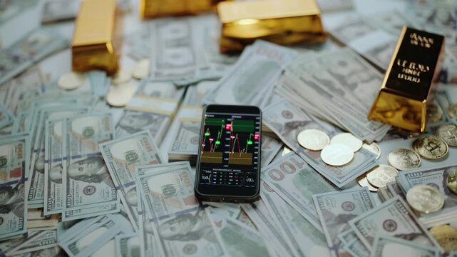 Modern smartphone displaying a live trading chart surrounded by one-hundred-dollar bills, shiny gold bars, and valuable coins, symbolizing wealth, investment, and financial market success