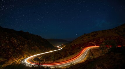 Night road with light streaks illuminating hills under starfilled sky suitable for travel and landscape visuals, brochures, and websites.