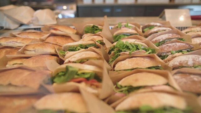 Freshly prepared sandwiches wrapped in paper on counter Large selection of sandwiches lined up in cafe display ready for sale