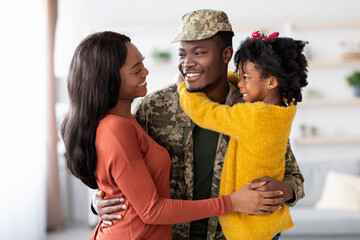 A soldier in uniform joyfully reunites with his partner and young daughter. They share smiles and hugs in a cozy living room, showcasing the warmth of family love and support.