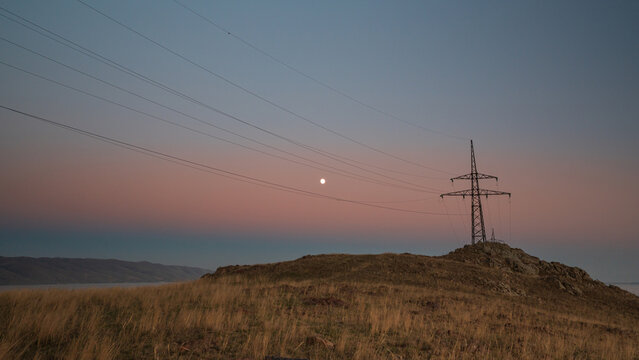An electric tower stands against a pastel sky at dusk near Lake Sevan. The power lines lead into the fading light, adding a modern contrast to the vast natural scene.