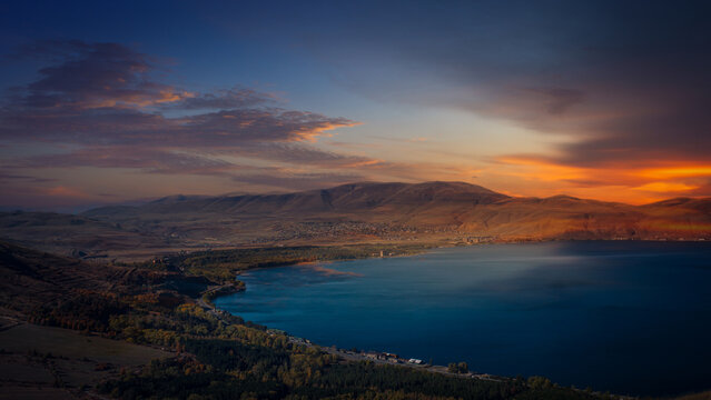 Serene evening scene over Lake Sevan surrounded by mountains, with warm colors of sunset reflecting on the tranquil surface.