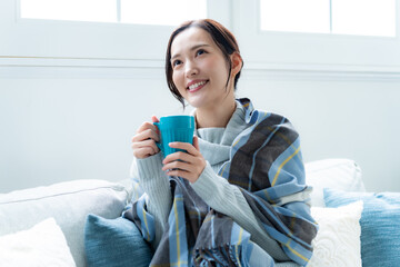 ソファでカップを持つ女性（癒し・おうち時間・ナチュラルな暮らし）