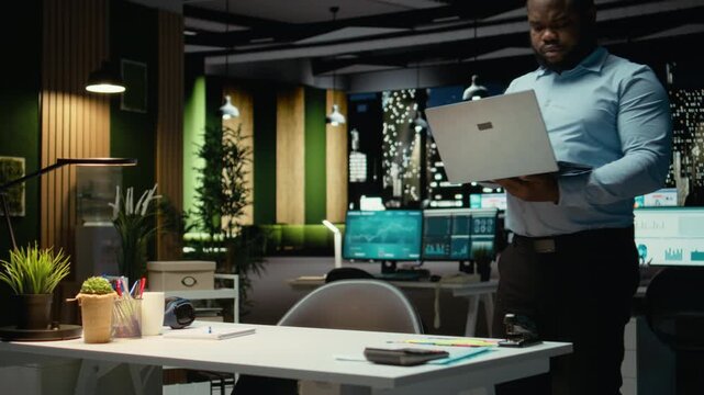 African american guy proofreading a document before transcribing on a textbook, extracting the main ideas from reports on laptop. Expert documenting after hours late at night. Camera A.