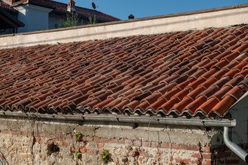 Detail of a building with a pitched roof covered with elegant terracotta tiles, with well-defined upper gable lines and ridge tiles, accompanied by a functional gutter.