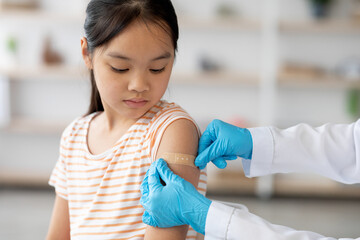 A young girl sits calmly while a healthcare professional applies a bandage to her arm after a...