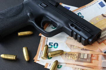 Close-up of black handgun with bullets and euro banknotes on dark surface, symbolizing crime, corruption, and illegal money.