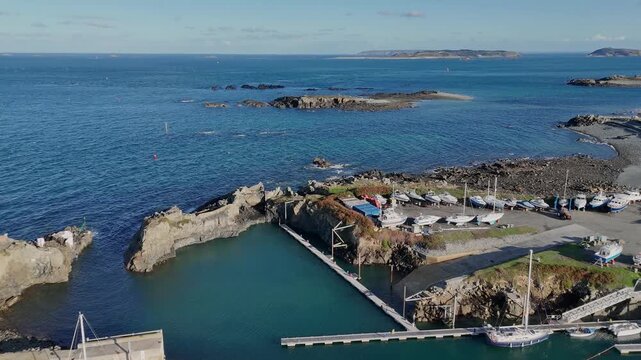 Flight over Beaucette Marina Guernsey in bright sunshine towards entrance views across to Herm and Jethou over rocky foreshore and outcrops to the Little Russell Channel