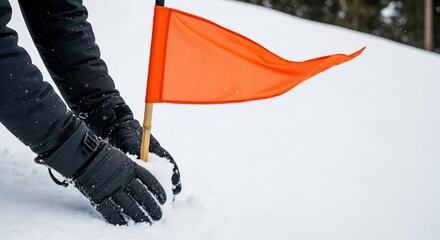 Hands in warm black winter gloves carefully planting a bright orange marker flag into fresh white snow on a cold, snowy day outdoors