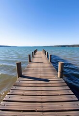 Naklejka premium Weathered wooden pier extending into a calm, vast lake under a clear sky, rustic, serene landscape