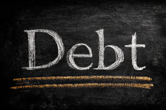 The word &ldquo;Debt&rdquo; written in white chalk on a blackboard, symbolizing education, awareness, and financial responsibility.