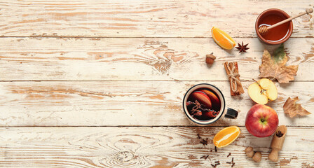 Cup of hot mulled wine with apple and orange on white wooden background