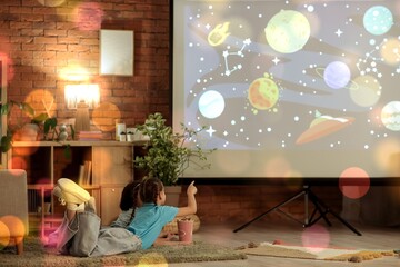 Cute girls with popcorn watching cartoons on projector screen at home in evening