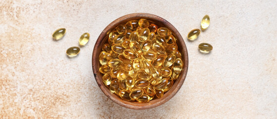 Wooden bowl with vitamin E capsules on light background, top view