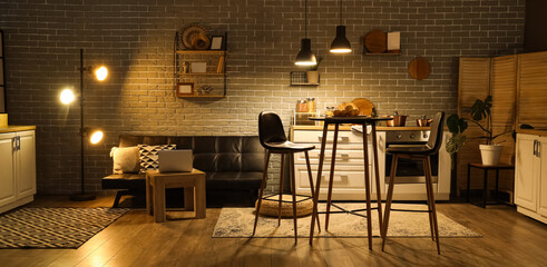 Interior of kitchen with counters, sofa and glowing lamps in evening