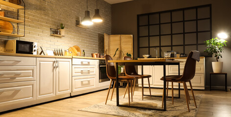 Interior of kitchen with counters, dining table and glowing lamps in evening
