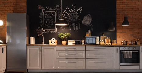 Interior of stylish kitchen with counters, chalk wall and glowing lamps at night