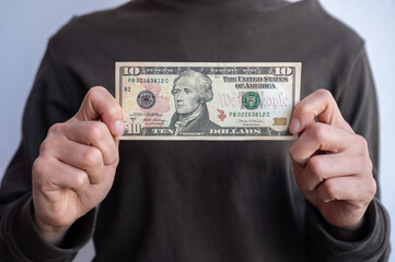 Cropped shot view of woman holding and showing ten American dollar banknotes in hands. The US Dollar is the currency of United States.