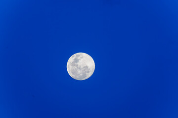 Circular moon with surface pattern center of image high in sky on blue background with copy-space,