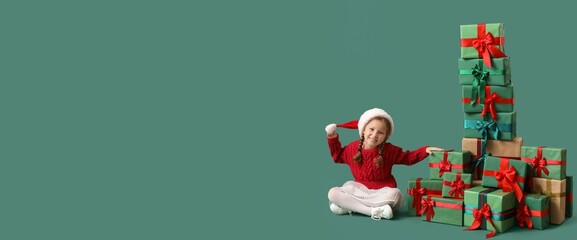 Cute little girl in Santa hat and with many Christmas presents sitting on green background with space for text