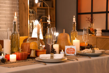 Beautiful table setting with burning candles, pumpkins and greeting cards for Thanksgiving dinner at evening