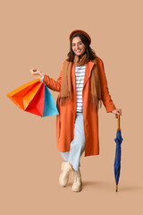 Young woman with shopping bags and umbrella on brown background