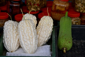 White jade bitter gourds with ridged texture and bumpy surface in dark basket with mesh padding, glass jars in soft-focused background, traditional market produce display, Taiwan.