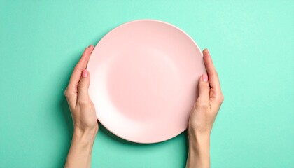 Hands holding empty pink plate, turquoise background, food concept