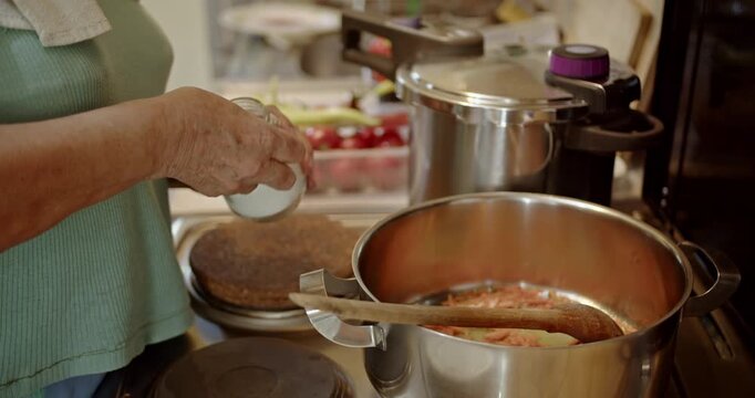 Watch as a woman's hands carefully add aromatic spices to a simmering pot of ingredients on the stove, bringing a delicious homemade meal to life in the kitchen.